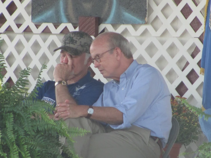 two older men sitting on a bench with one holding his head in his hands