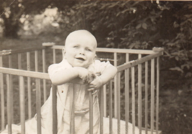 an old black and white pograph of a child leaning on a gate