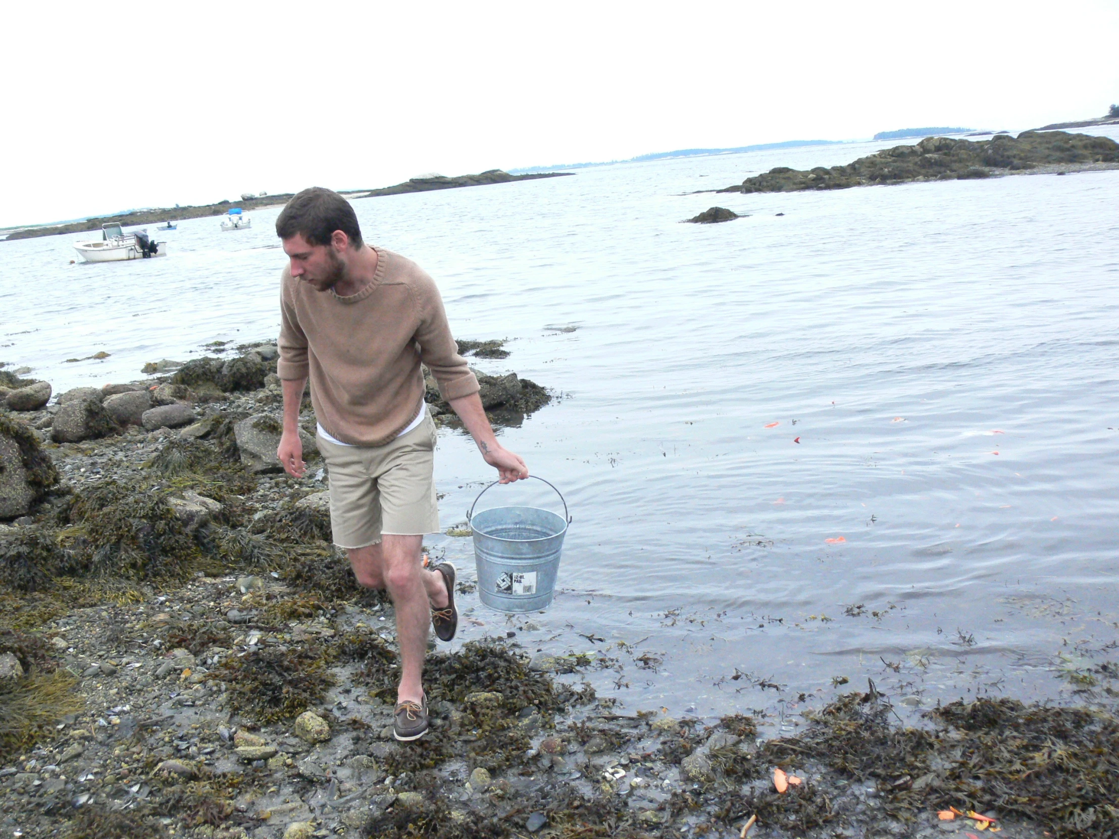 a man walking into the water with a basket and fish