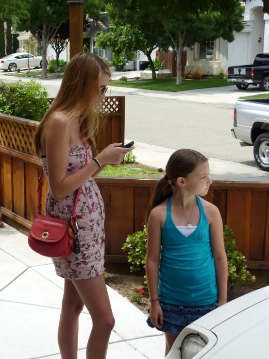 two girls looking at their cell phones next to the back of a car