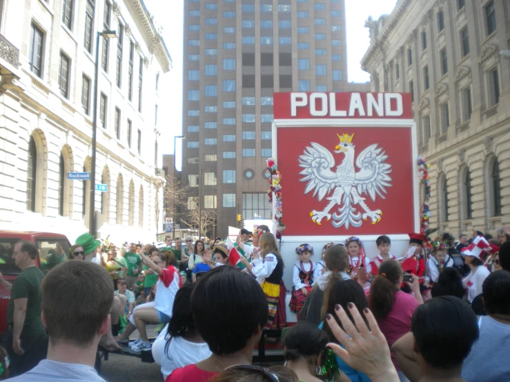 people on street with large polish sign in the middle