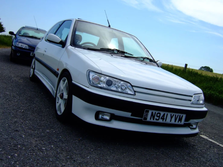 two white cars on a road with grass in the background