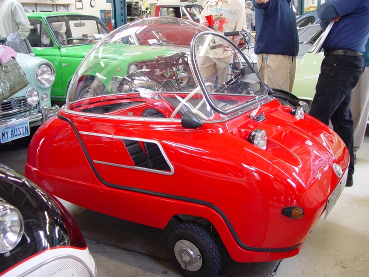 a small red car sits on display with some people in the background