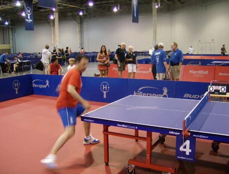 a man wearing red shirt playing table tennis on a blue ping pong court