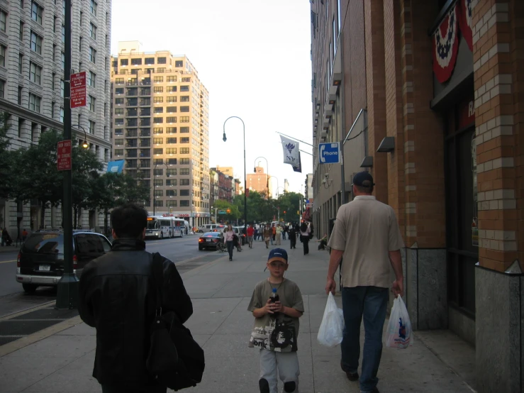 three people walk down a street with tall buildings in the background