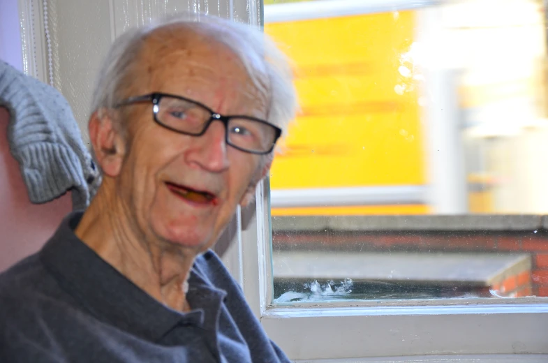 an old man with glasses smiling looking out a window