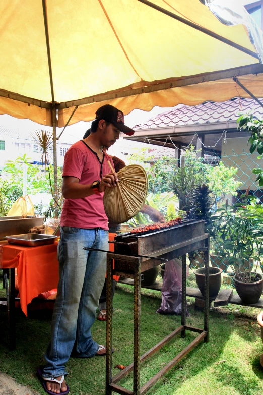 a man holds a large bamboo fan under an umbrella