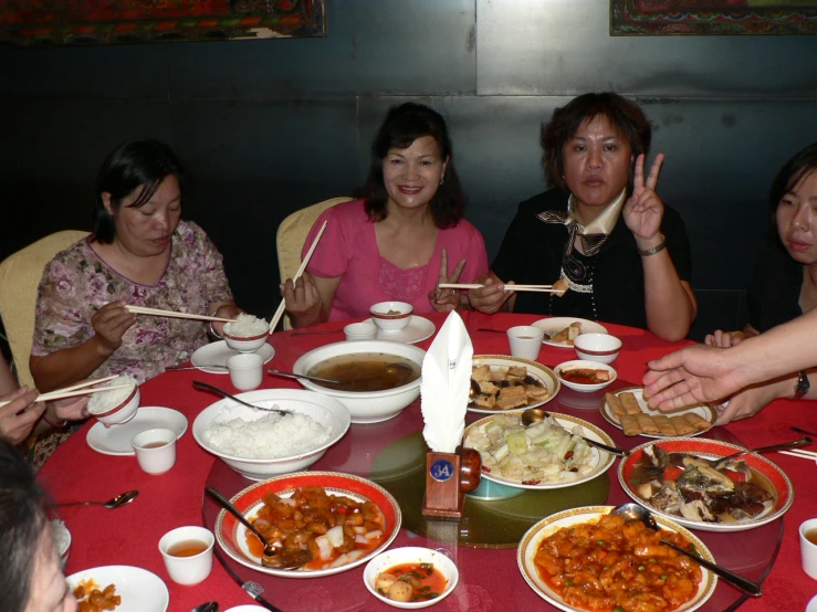 five women sit at a table that is covered with dishes and bowls, holding chop sticks up to signifying that there is plenty of food on the plate