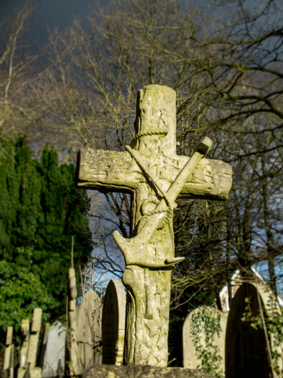 an old green cemetery stone cross with a tree in the background