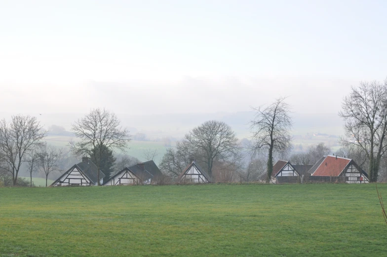 a po of a green landscape with three small wooden buildings and some trees