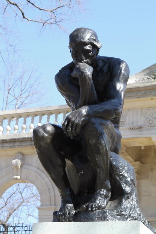 a statue with its hand on his chin next to a building