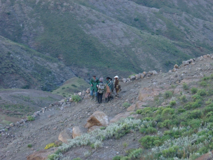 people hiking up a mountain side trail with bags