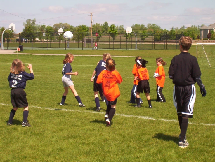 girls in orange uniforms are playing soccer on the field