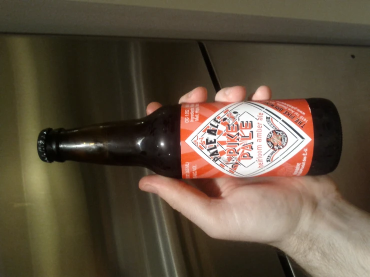 an arm holding a beer in front of a refrigerator