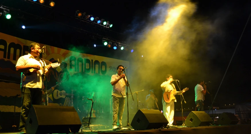 three men stand on stage while performing at an outdoor concert