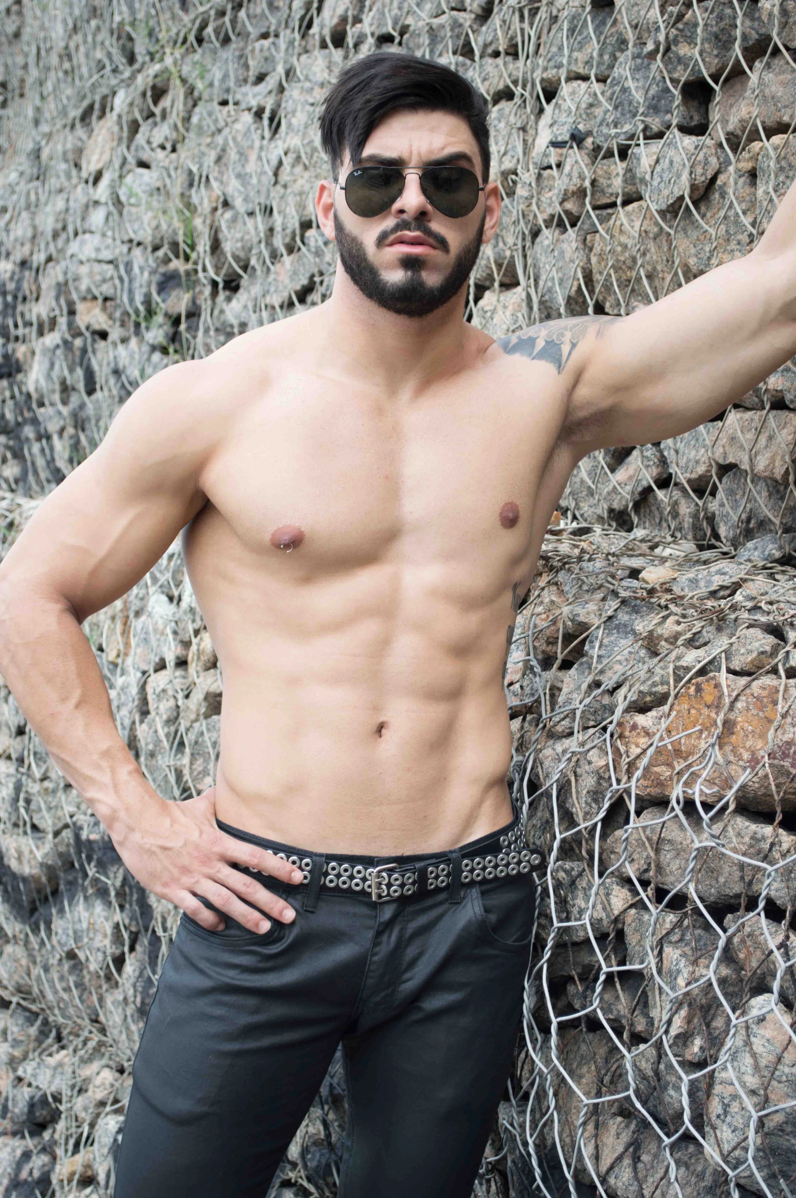 a man with sunglasses standing by rocks wearing black pants