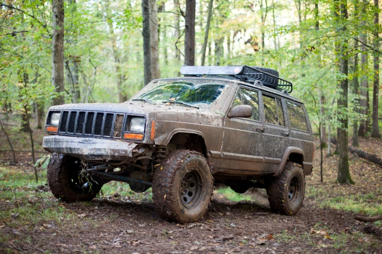 a muddy, dusty jeep parked on a trail in the woods