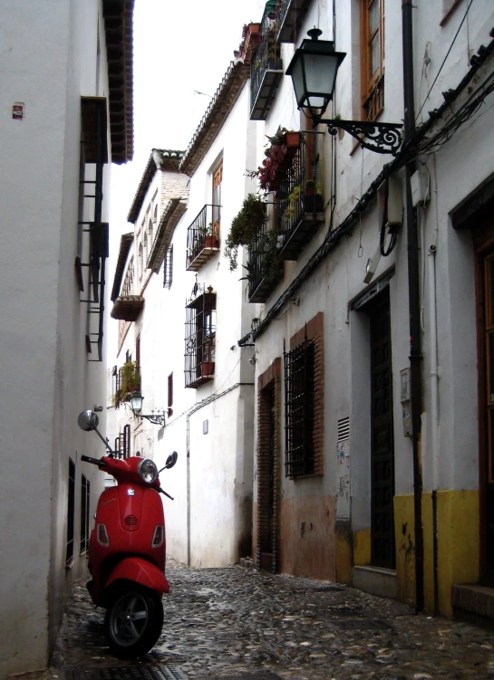 red scooter parked on the side of a narrow street in a city