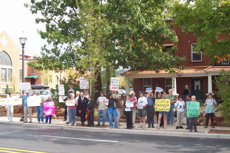 many people standing outside holding signs by the side of the road