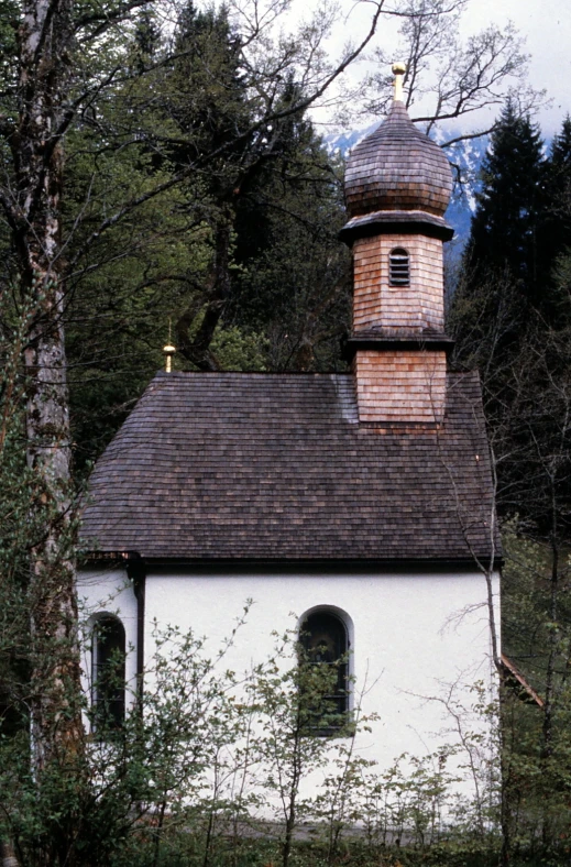 a very small church by some trees with a clock