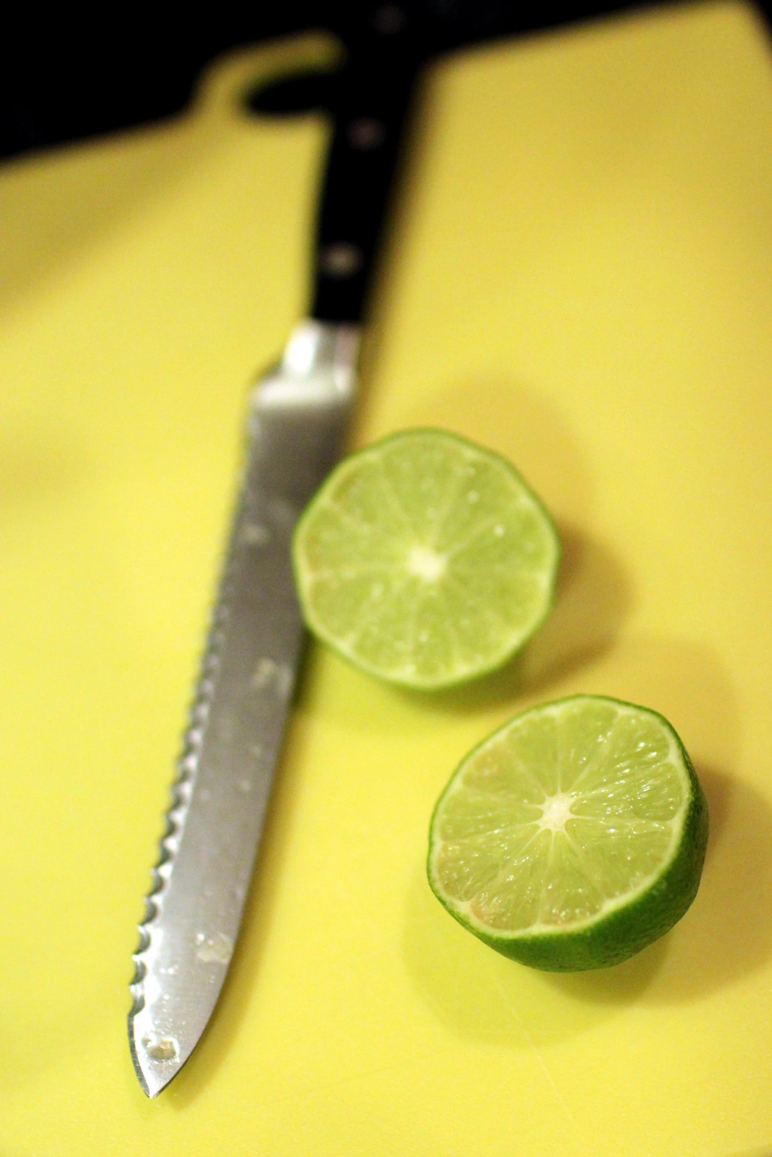 limes cut in half on yellow  board with knife