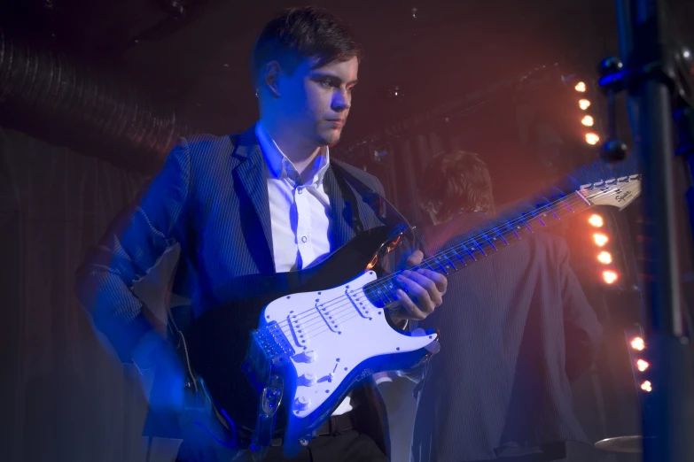 a young man plays on his white electric guitar