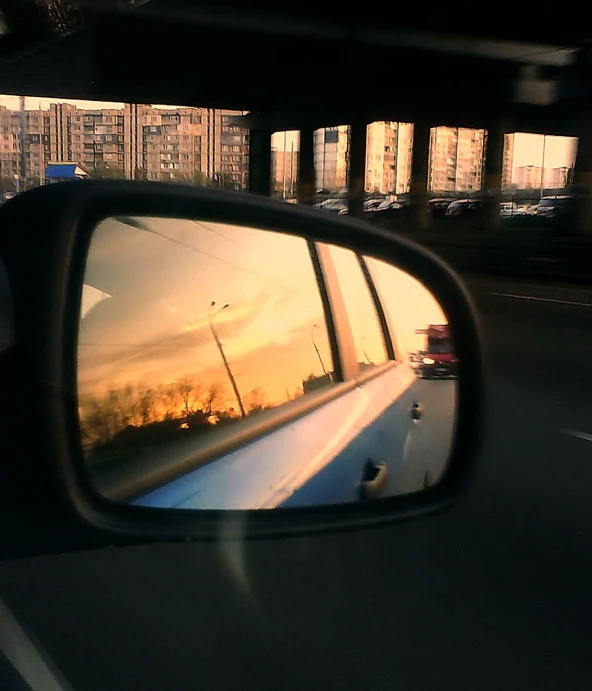 the rear view mirror reflects a sunset on the side of a bus