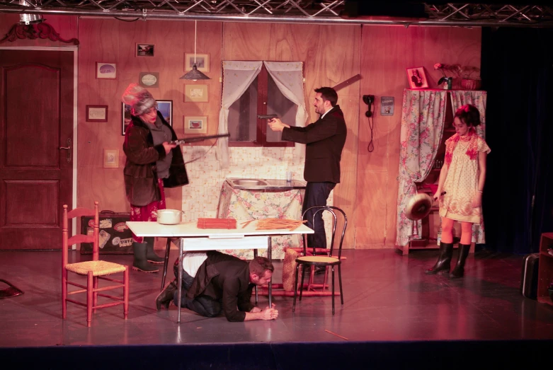 people stand in a stage set with a table and chairs