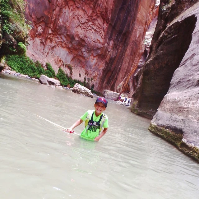 a  walking in shallow water at the base of a steep gorge