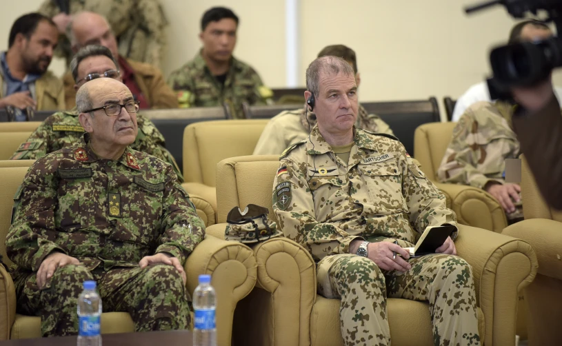 military men sitting in chairs with cameras in the background