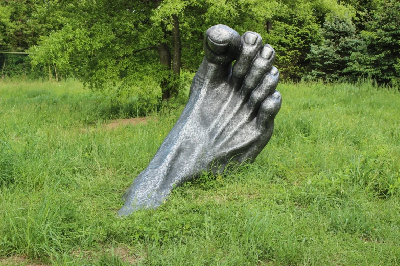 a large foot statue sitting on top of a lush green field