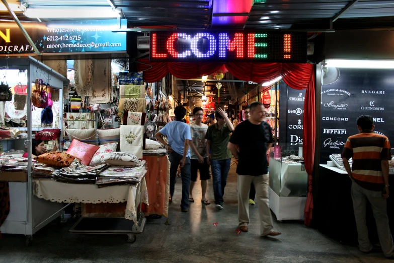 people walking through a street vendor market with signs above the vendors tables