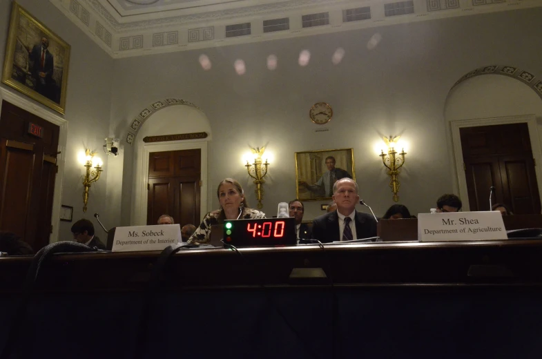 two men and a woman in suits sit at a table with signs that says 3 am, and a clock