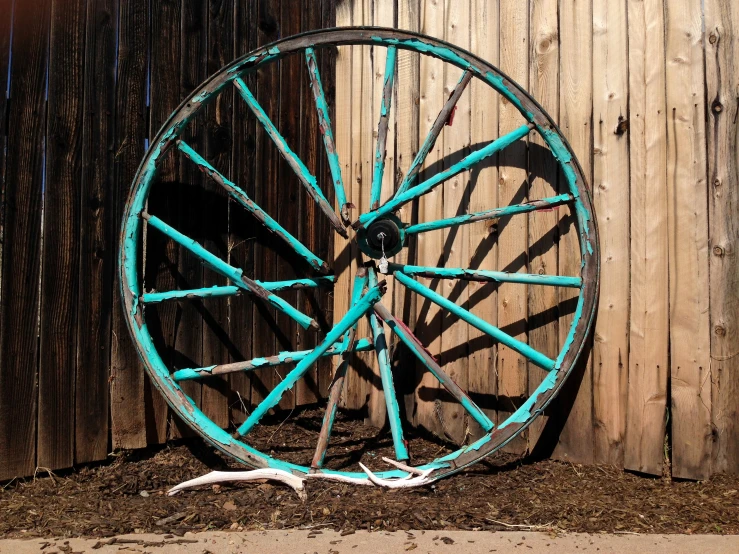 a very old wheel leaning up against a fence