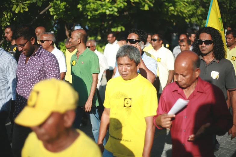 several people with yellow shirts and one with grey hair walk past others