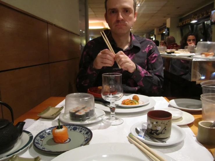a man in a restaurant holding two chop sticks over his eyes