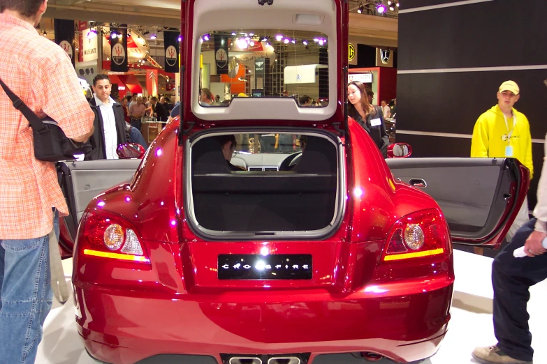 several people standing around a show room with a red car