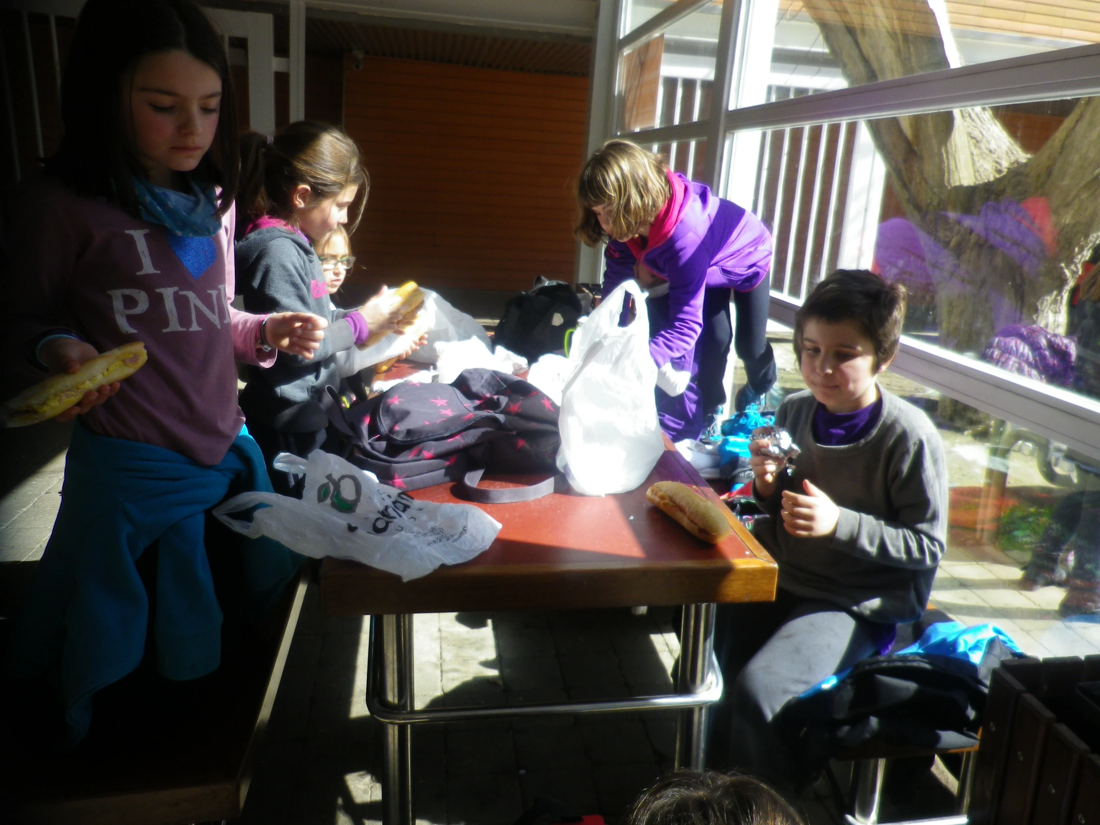 children stand at the end of a table that has some bags sitting on it