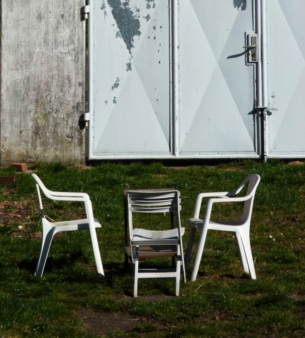 three white chairs sitting outside near a shed