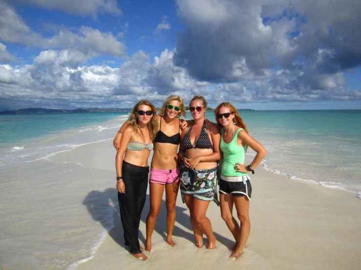 three girls and one is wearing sun glasses standing by the ocean