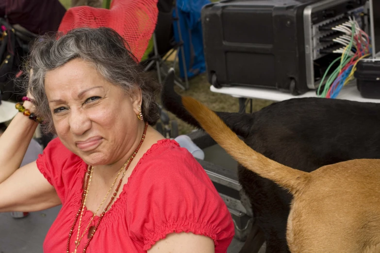a woman wearing a red top and smiling at the camera, with a brown dog walking nearby