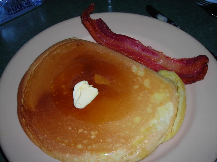 there is a piece of bacon next to some pancakes