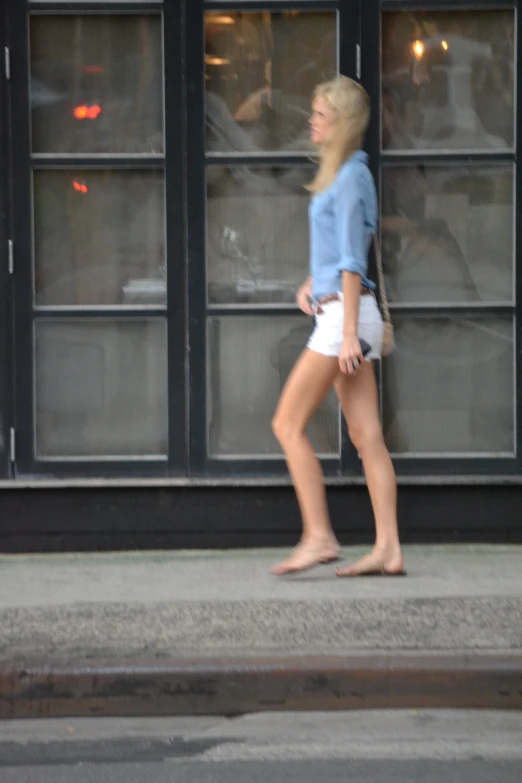 a blonde woman in white shorts walking down the sidewalk