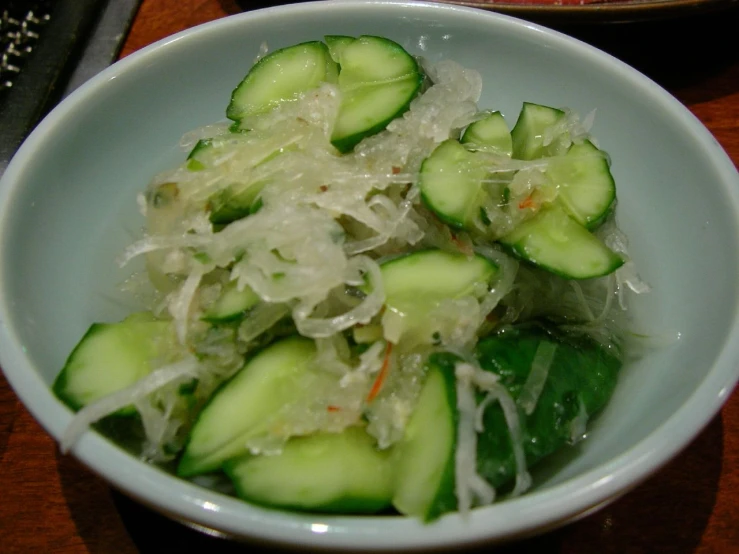 a white bowl containing a salad of cucumbers