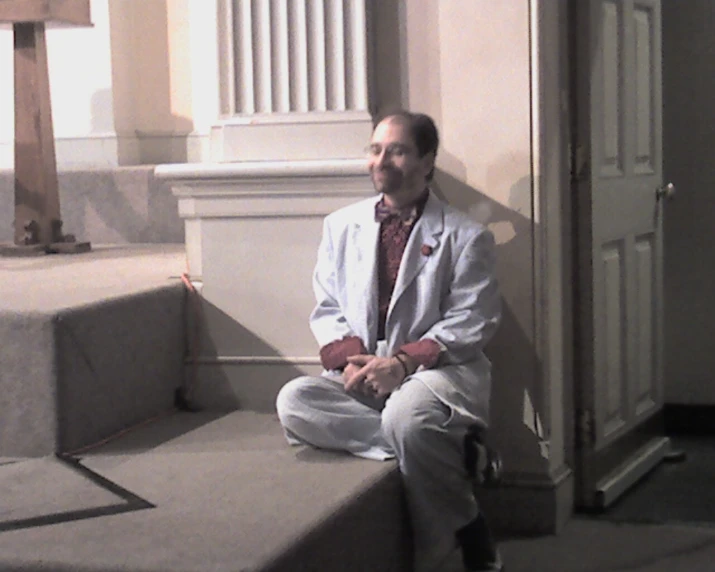 a man with a white jacket and tie sitting on steps