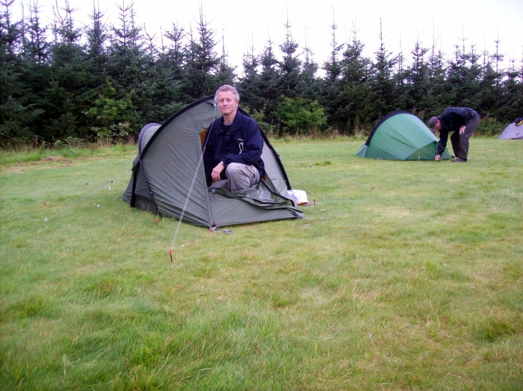 a man sitting in his camping tent at the edge of a field