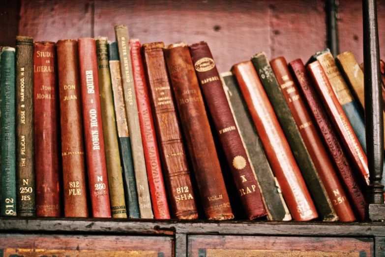 a row of old books sit on top of a book case