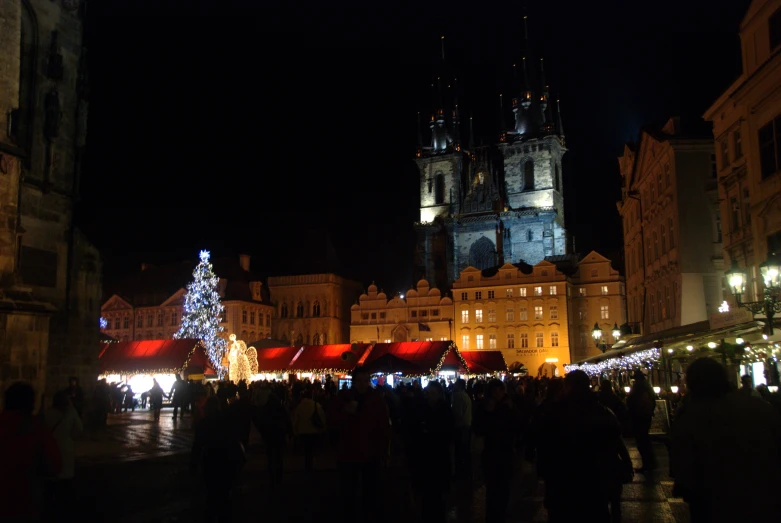 a christmas tree surrounded by crowds in front of an old fashioned clock tower