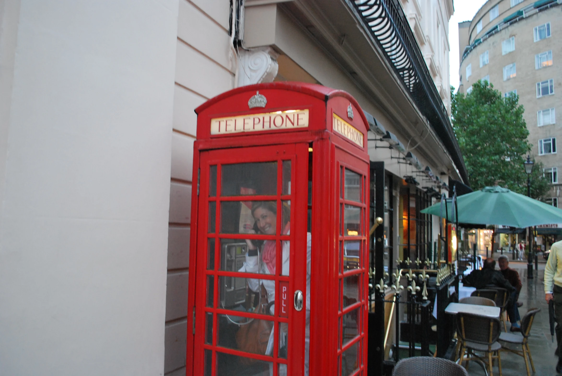 people sitting in a red telephone booth on a sidewalk