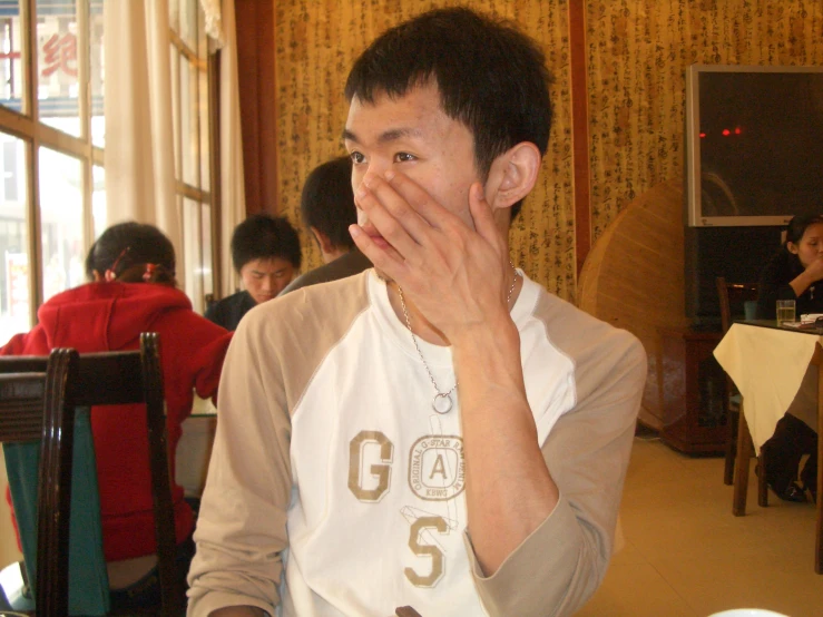 an asian man covering his face in front of a window